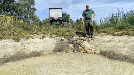 Ein Mann steht vor einer Wasserstelle, mit einem Wassertank im Hintergrund