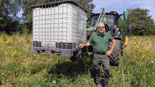 Ein Mann steht vor einem Traktor, welcher einen Wassertank hebt