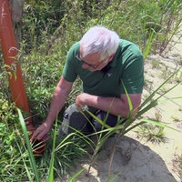 Ein Mann kniet vor einem Wasserrohr, dass ean einen Weidezaun gelehnt ist. 