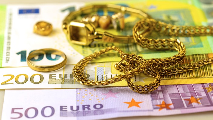 Symbolbild: Goldschmuck liegt auf Geldscheinen.
