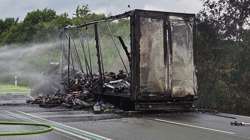 Ein ausgebrannter Lkw, der mit Wasser besprüht wird.
