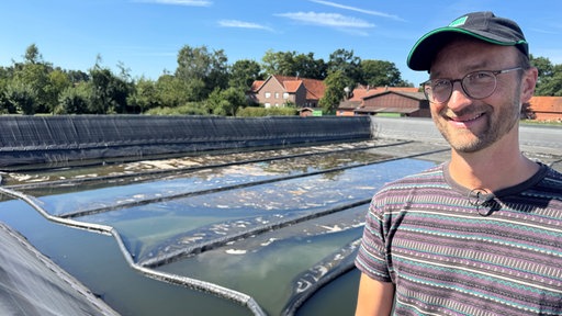 Ein Mann mit Mütze und Brille steht vor einem großen Regenauffangbecken