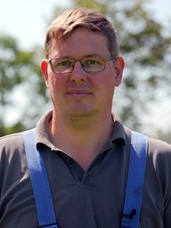Ein Mann mit Brille und braunen Haaren steht in einem Feld