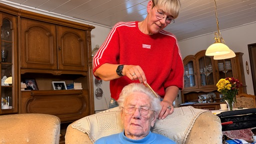 Die pflegende Tochter kämmt ihrer Mutter die Haare.