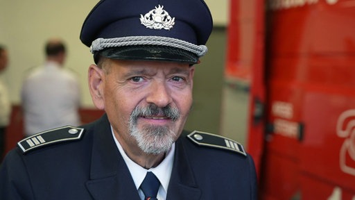 Dieter Krawitz schaut in seiner Uniform in die Kamera und im Hintergrund steht ein Feuerwehrwagen.