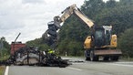 Ein Bagger greift nach den gelöschten Wrackteilen auf der Fahrbahn