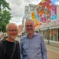 Zwei Männer stehen in einer Fußgängerzone vor Streetart auf einer Hauswand