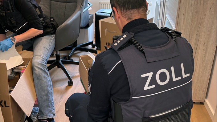 Zollbeamte durchsuchen mehrere Kisten mit u.a. Dokumenten.