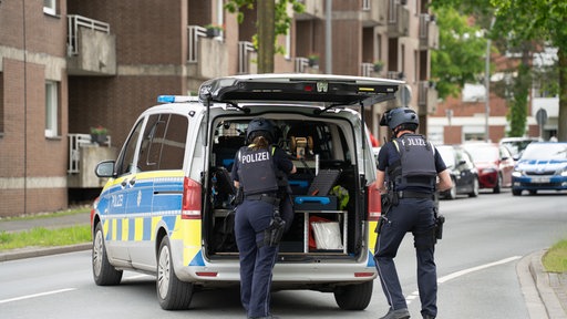 Zwei Polizisten vor einem Polizeiwagen.