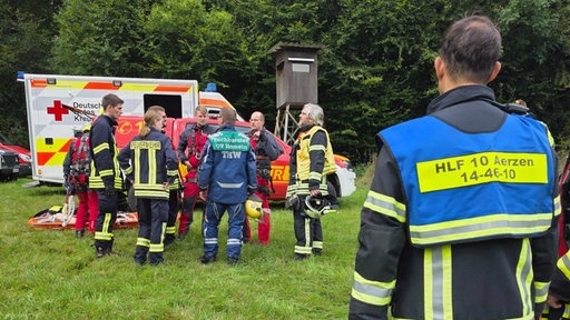 Die THW, Feuerwehr und das Deutsche Rote Kreuz stehen vor ihren Einsatzfahrzeugen am Einsatzort im Wald.