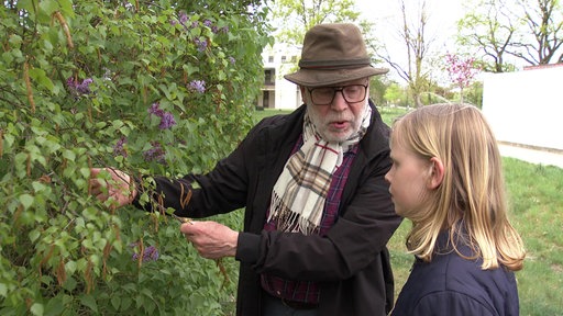 Ein Mann zeigt einem Mädchen eine Pflanze in einer Hecke
