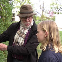 Ein Mann zeigt einem Mädchen eine Pflanze in einer Hecke
