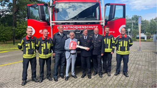 Innenminister Reul steht mit Feuerwehrmännern vor dem neuen Waldbrand-Tanklöschfahrzeug.