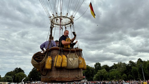 Korb eines Heißluftballons kurz nach dem Start mit Menschen drin.