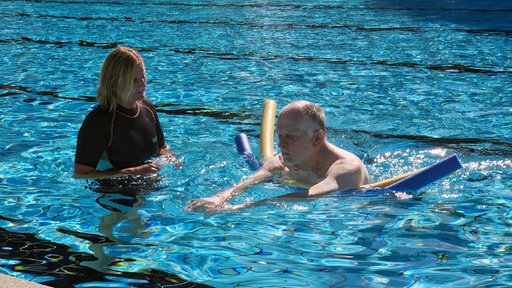 Die Schwimmtrainerin schaut ihrem älteren Schüler im Wasser beim Schwimmen mit Schwimmnudeln zu