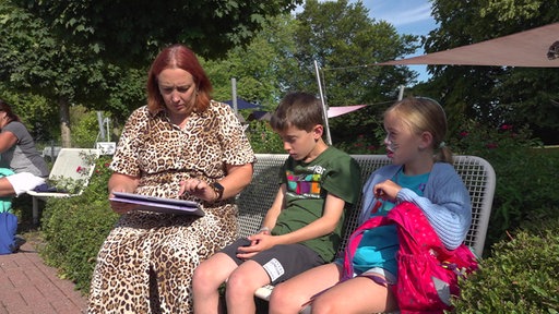 Tanja Vrenken sitzt im Freibad mit ihren Kindern auf einer Bank und schaut auf die Petition in ihrem Tablet.