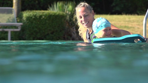Schwimmlehrerin Christina Wöhle bringt einem Kind im Wasser mit einem Schwimmbrett schwimmen bei.