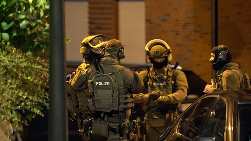 SEK-Beamte stehen in voller Ausrüstung im Kreis bei Nacht.