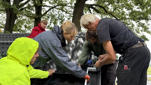 Vier Personen sind auf einem Dach und bringen ein Solarpanel an