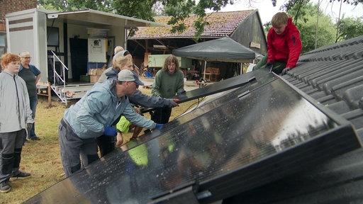 Mehrere Personen installieren ein Solarpanel auf einer Übungs-Dachkonstruktion.