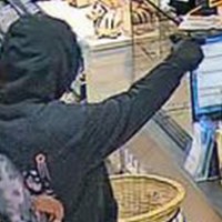 Vermummter Mann mit einem schwarzem Hoodie und einer Pistole.