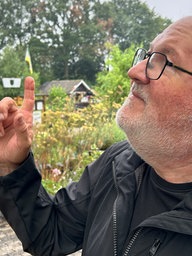 Ein Mann mit Brille zeigt in den Himmel