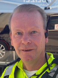 Polizist Michael Volmer, im Hintergrund steht ein Anhänger mit einem kaputten Unfallauto.