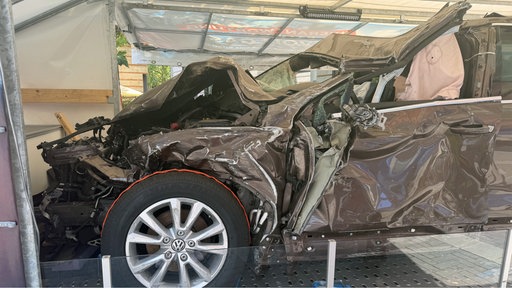 Ein braunes, kaputtes Auto, dessen komplette Motorhaube, Seite und vorderes Dach verformt ist.