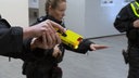 Die Hand eines Polizeibeamten hält einen gelben Taser einsatzbereit.