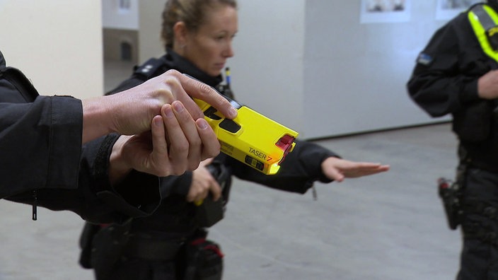 Die Hand eines Polizeibeamten hält einen gelben Taser einsatzbereit.