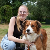 Eine Frau lächelt kniend in die Kamera und streichelt dabei einen Hund.