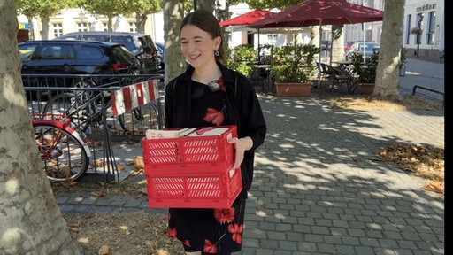 Sophia Wolf hält eine rote Kiste voller Briefe in der Hand und läuft damit über den Marktplatz