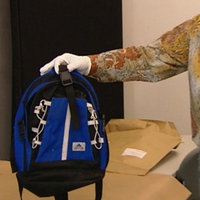 Ein blauer Adidas-Rucksack wird von einem Ermittler in der Hand gehalten.