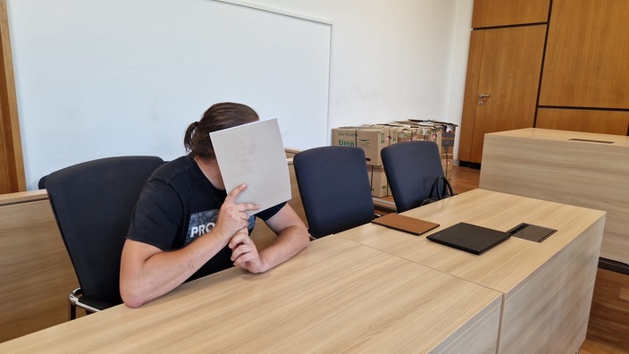 Angeklagte Person hält sich Einen Block vor das Gesicht