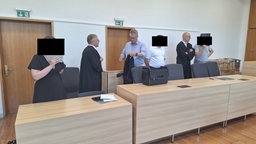 Sechs Personen, Zwei in Talar, Zwei andere halten sich Ordner vor das Gesicht
