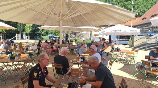 Menschen sitzen in einem Biergarten an Tischen