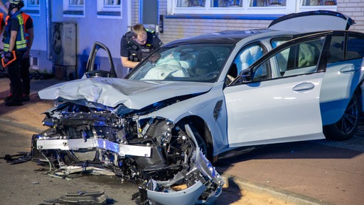 Eun Auto vor einer Hauswand. Der Motor vorne ist zerstört. Ein Polizist begutachtet den Schaden.