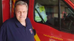 ein Mann von der freiwilligen Feuerwehr steht in Dienstkleidung vor einem roten Einsatzwagen