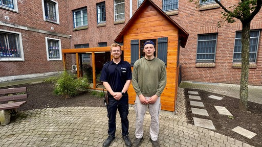 Justizvollzugsbeamter Marius Int-Veen und Inhaftierte Maxim stehen vor der Vogelvoliere.