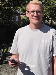 Junger Mann steht auf dem Marktplatz in Walbeck und schaut auf sein Smartphone, hat keinen Mobilfunkempfang.
