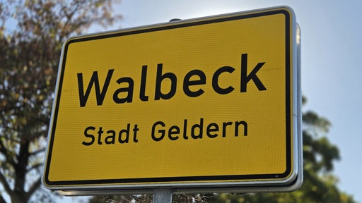 Gelbes Ortseingangsschild mit der Aufschrift „Walbeck“ am Straßenrand.