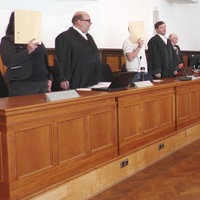Angeklagte, ihre Verteidiger und Richter stehen im Gerichtssaal.