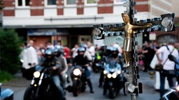 Kreuz mit Jesus-Statue im Vordergrund, unscharfe Motorräder im Hintergrund.