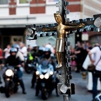 Kreuz mit Jesus-Statue im Vordergrund, unscharfe Motorräder im Hintergrund.