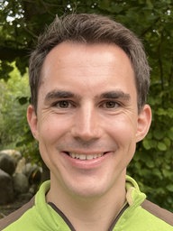 Martin Polotzek (Leiter des Klever Tiergartens) steht draußen im Grünen, grinst und trägt einen braun-grünen Pullover.