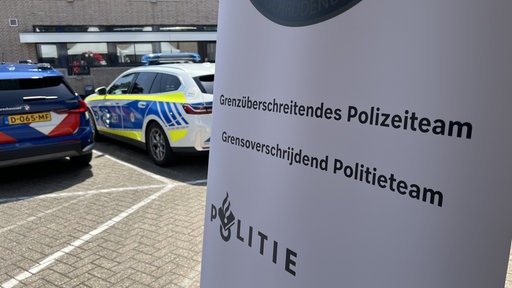 Schild mit der Aufschrift "Grenzüberschreitendes Polizeiteam" und Polizeiautos