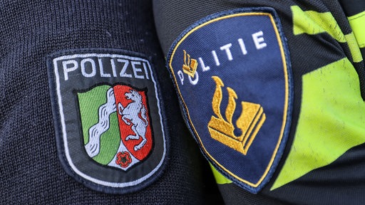 Die Wappen der deutschen und niederländischen Polizei auf zwei Uniformärmeln nebeneinander