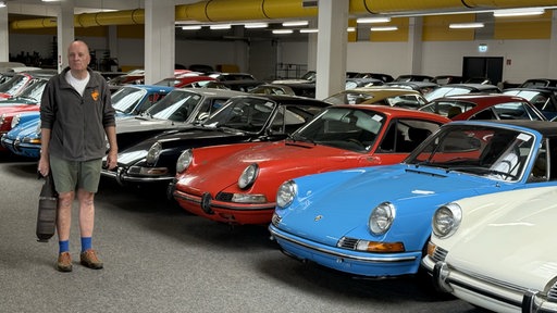 Andreas Schulz steht vor seinen Porsche Oldtimern in seinem Lager