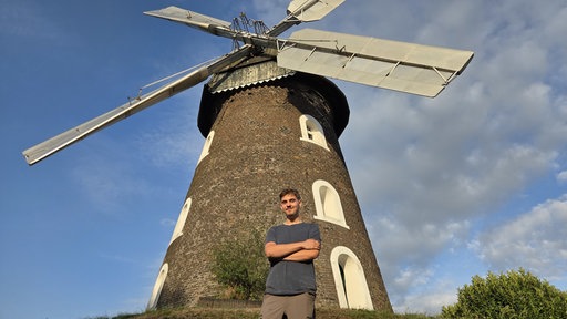 Ein junger Mann steht vor einer Mühle