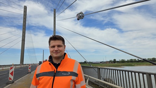Leonard Schulte-Hammerschmidt steht auf der Rheinbrücke in Rees hinter ihm das Rheinufer.